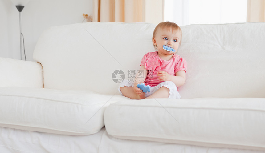 可爱的金发美女宝宝在玩拼谜游戏的同时坐着长椅女孩家庭沙发房间白色乐趣女儿生活儿童图片