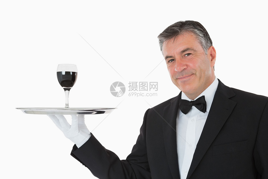 在银盘上拿着一杯酒的笑脸服务员套装领结服务衬衫白色玻璃平衡男性奢华头发图片