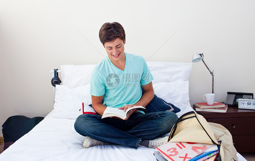 微笑的少年在卧室里读一本书图片