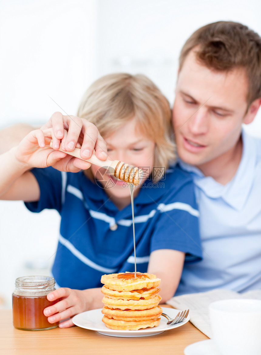 笑男孩和他父亲把蜂蜜放在华夫饼上图片