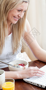 在吃早餐时使用笔记本电脑的开心女人技术高清图片素材