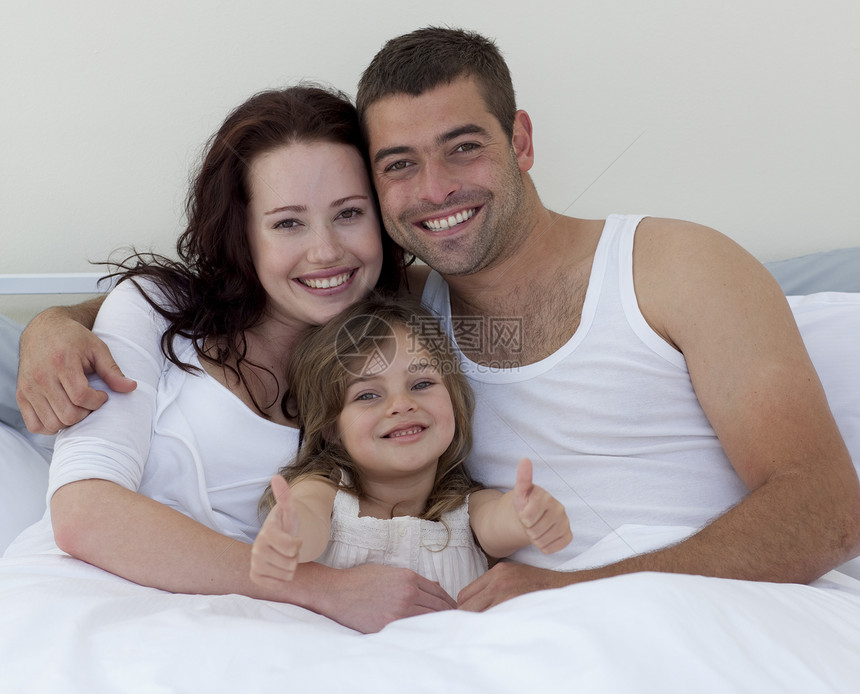 幸福的年轻家庭躺在床上 举起拇指图片