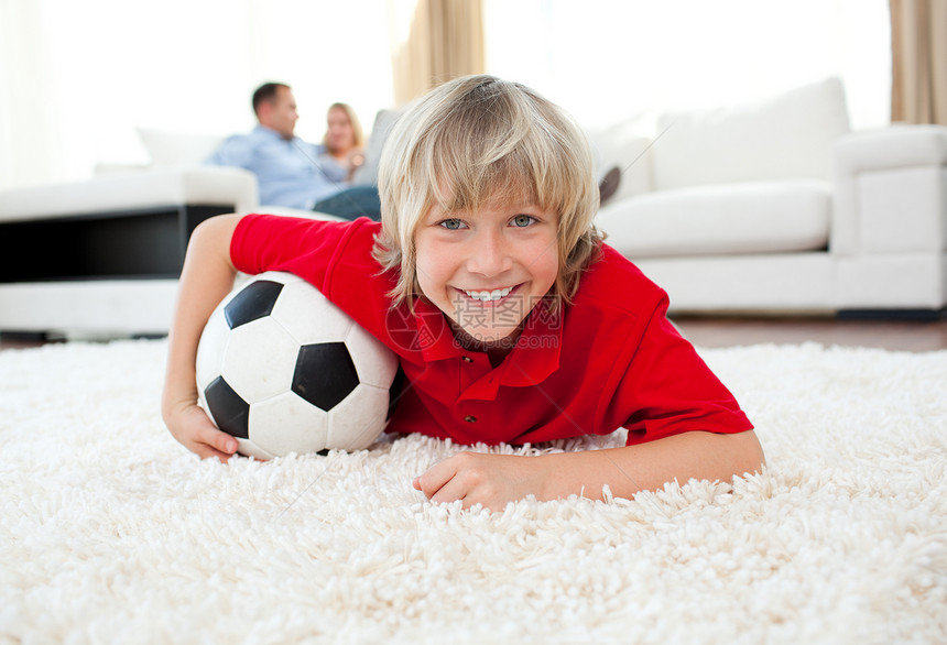 微笑的男孩看足球比赛 躺在地板上图片