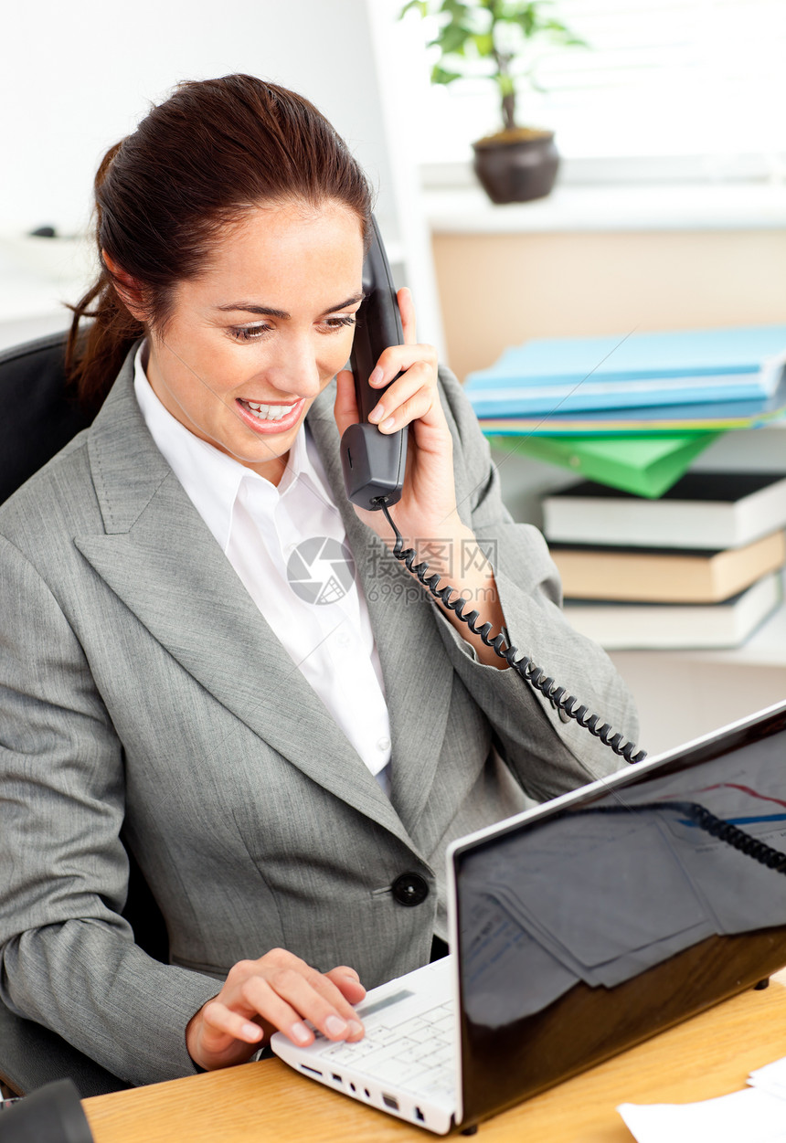 忙碌的女商务人士在电话上说话 并使用她的笔记本电脑图片