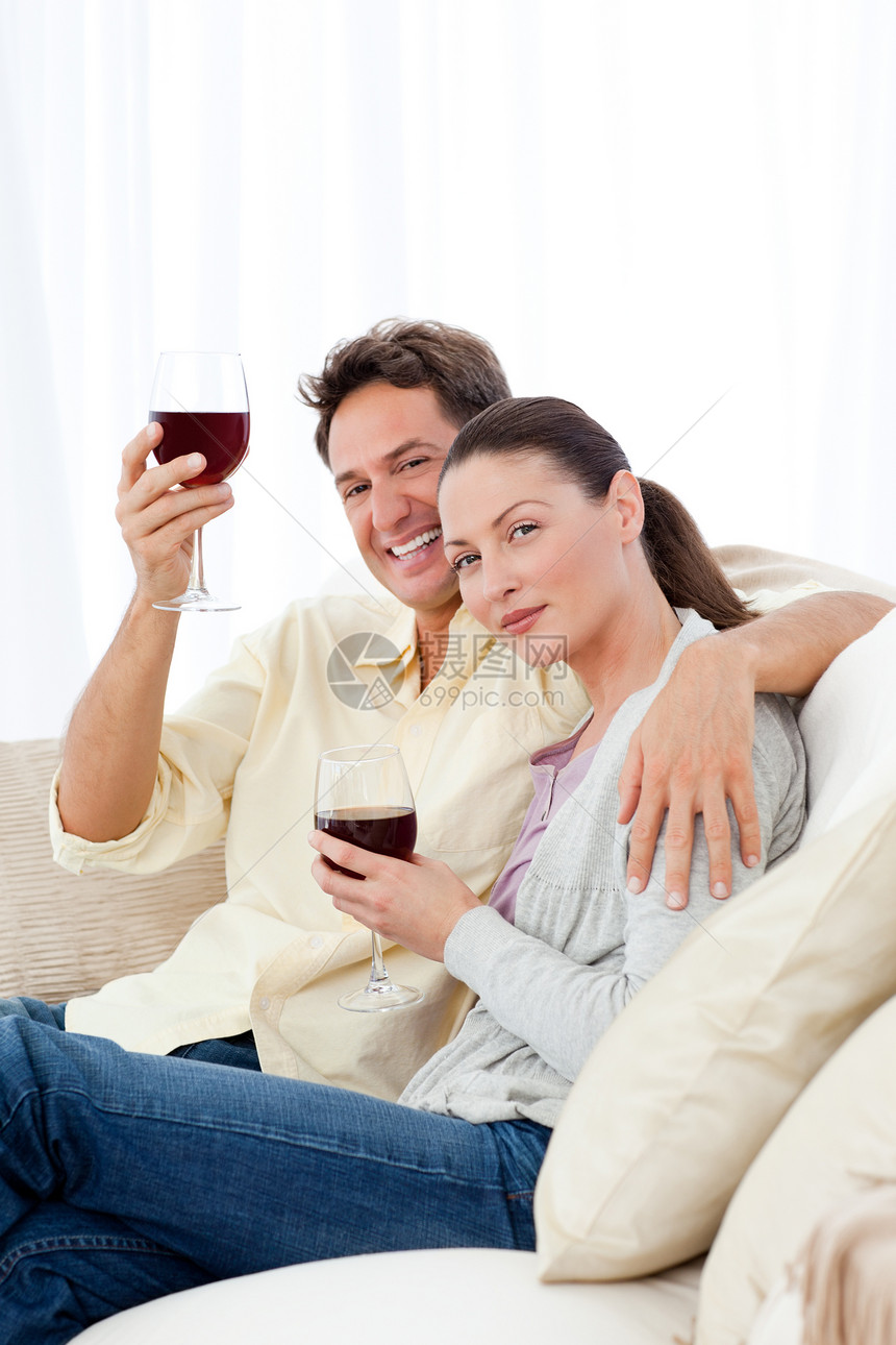 快乐的情侣在沙发上享受着他们的红酒杯图片