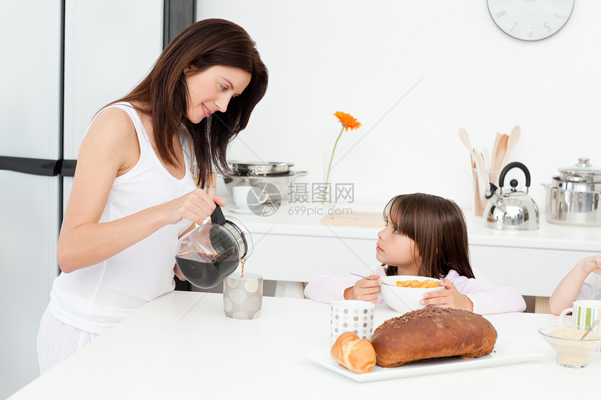漂亮妈妈在孩子吃早饭时倒咖啡 而她的孩子正在做早餐图片