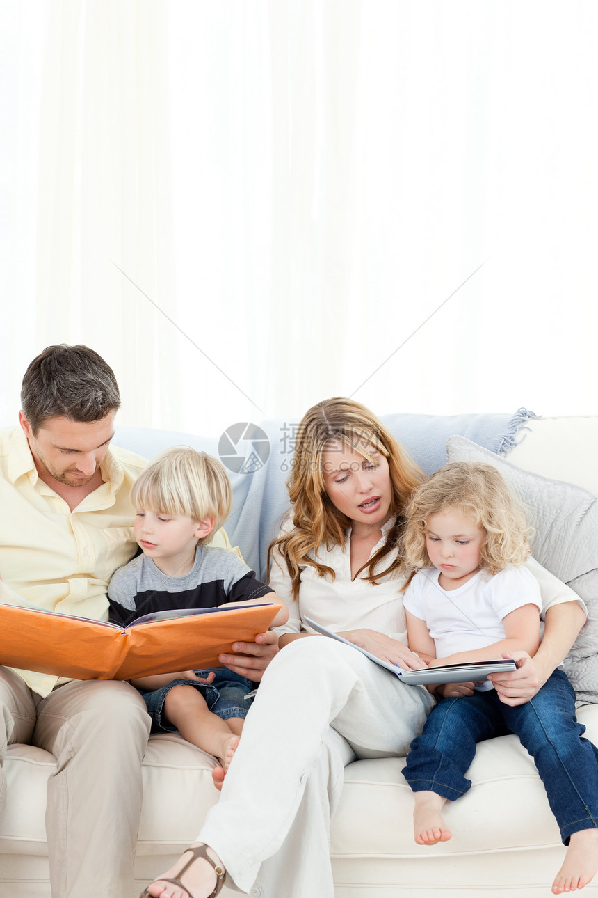 家人在沙发上读书孩子男孩们女性拥抱微笑父母家庭女孩们阅读图书图片