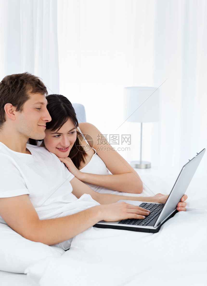 年轻夫妇在家电脑上观看视频的年青夫妇幸福网络女士微笑技术快乐家庭卧室男性情人图片