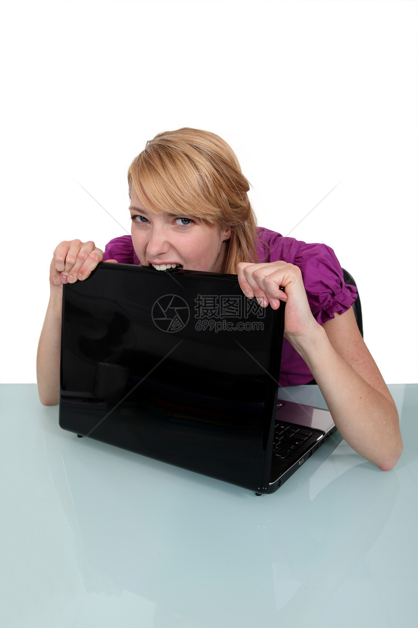 年轻妇女咬她的笔记本电脑图片