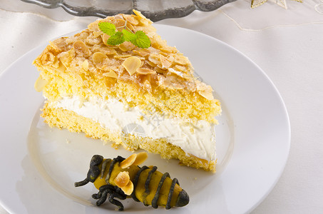 蜂蜜奶油蛋糕带有杏仁和糖涂层以及奶油或奶油的扁蛋糕牛奶甜点糕点蜜蜂蜂蜜派对咖啡蜡烛桌子香草背景