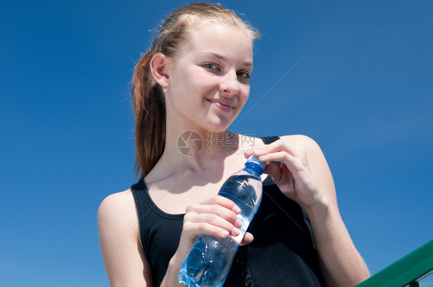 年青妇女锻炼后饮用饮用水成人长发活力女性闲暇蓝色瓶子太阳女孩深色图片