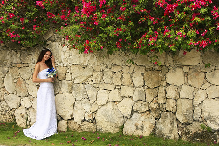 穿着婚纱的年轻女士 在石墙前摆着热带花朵婚礼订婚微笑新娘戒指女孩裙子头发长的高清图片素材
