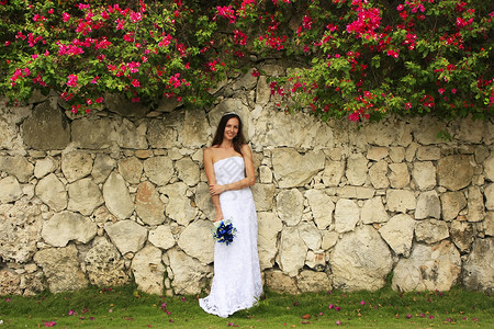 穿着婚纱的年轻女士 在石墙前摆着裙子热带婚礼女孩订婚冒充新娘花束头发黑发花朵高清图片素材