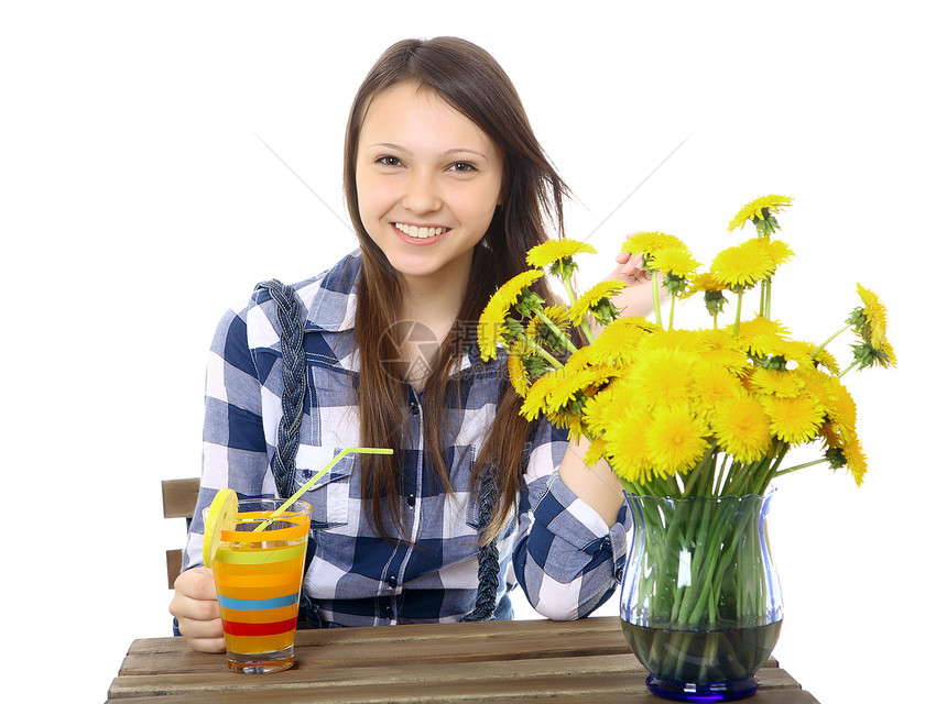 十几岁的女孩 白人外貌 黑发 穿着格子衬衫 拿着一杯饮料 桌子上有一个蓝色的花瓶 上面放着一束黄色的野花 蒲公英图片