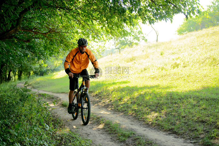 赛车手骑着自行车在森林的铁轨上旅行橙子山地踪迹绿色草地成人速度头盔黄色图片