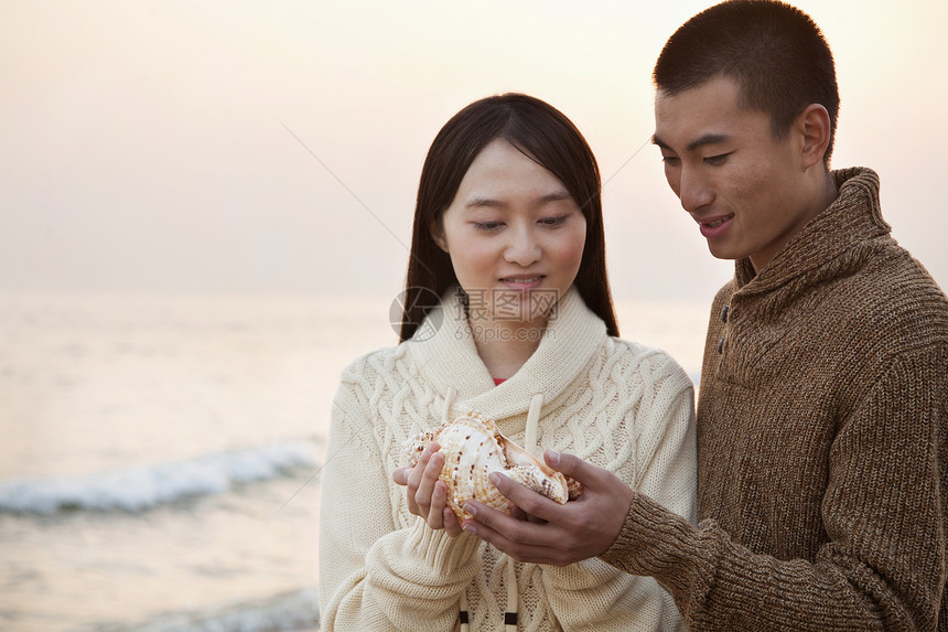 环贝壳的年轻夫妇日落目的地旅游海浪女朋友海洋年轻人沉思海滩休闲图片