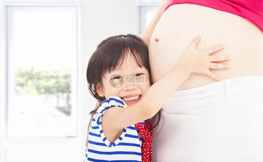 快乐的小女孩拥抱一个怀孕母亲的腹部图片