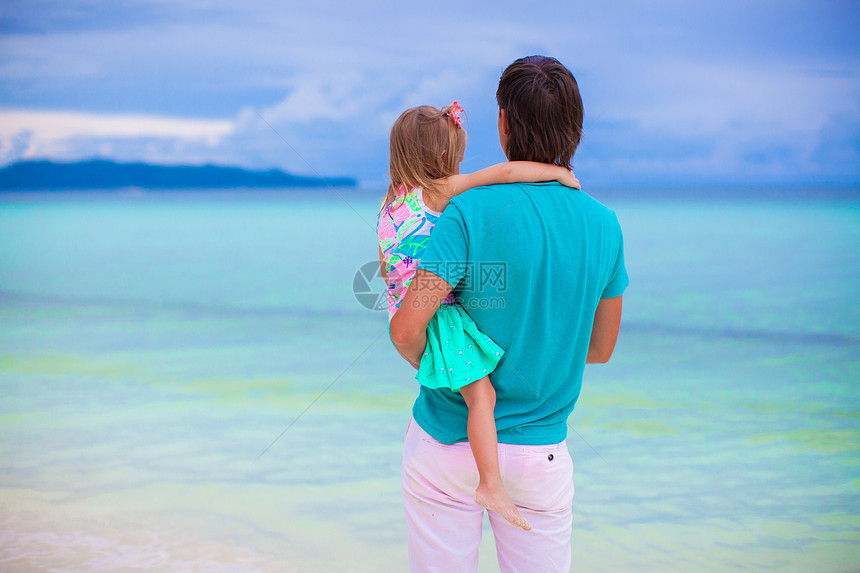 父亲和他的小女儿在热带海滩的海边观望着图片