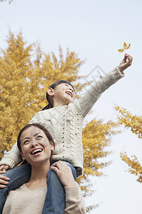 女儿骑着小猪背坐在母亲的肩上享受秋季假期收腰摄影妈妈团结乐趣家庭快乐衣物活动情绪微笑高清图片素材