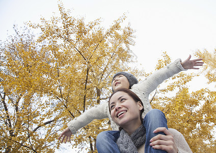 母亲和女儿双臂伸展 周围环绕着秋树爱高清图片素材