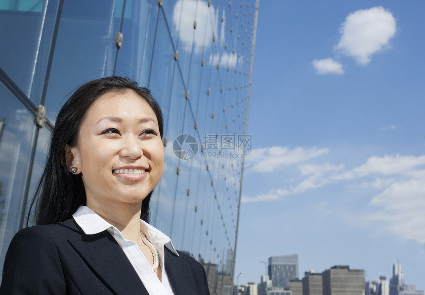 在玻璃楼前的外边 年轻笑着的女商务人士图片