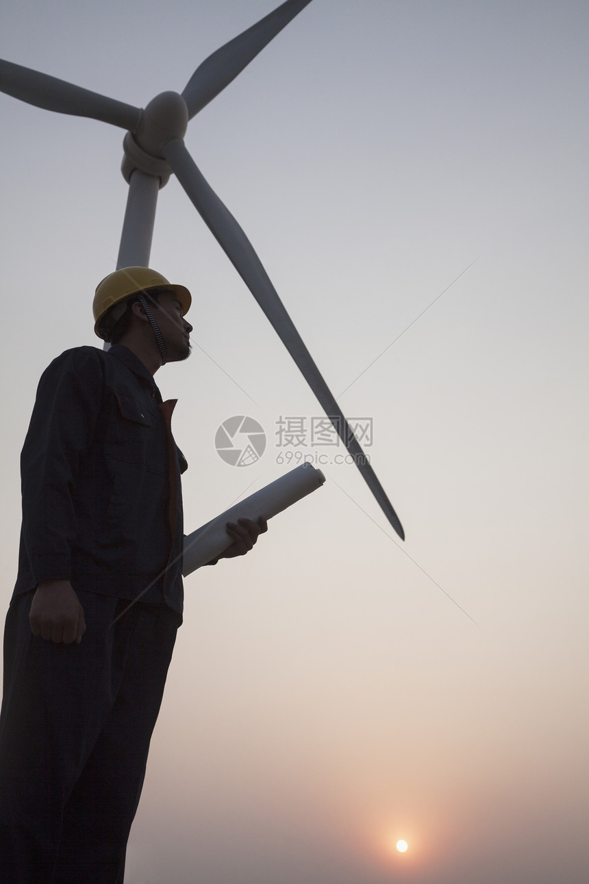 年轻男性工程师持有蓝图 在日落时站在风涡轮机旁边的青年男子工程师月光环境保护摄影涡轮机发电年轻人能源安全帽风力环境天空图片