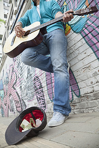 年轻街头音乐家在墙前用涂鸦弹吉他和抢车赚钱背景图片