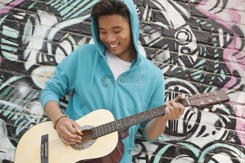 年轻 笑着的街头音乐家靠在墙上 涂鸦画画和弹吉他文化幸福演员娱乐享受摄影城市生活活动吉他乐趣图片