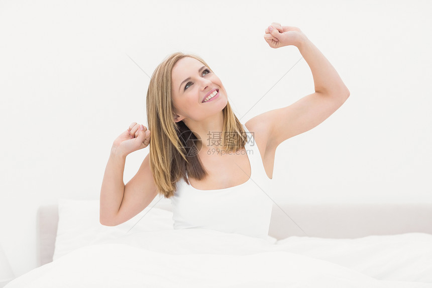 微笑的女人在床上醒来 伸起双臂来图片