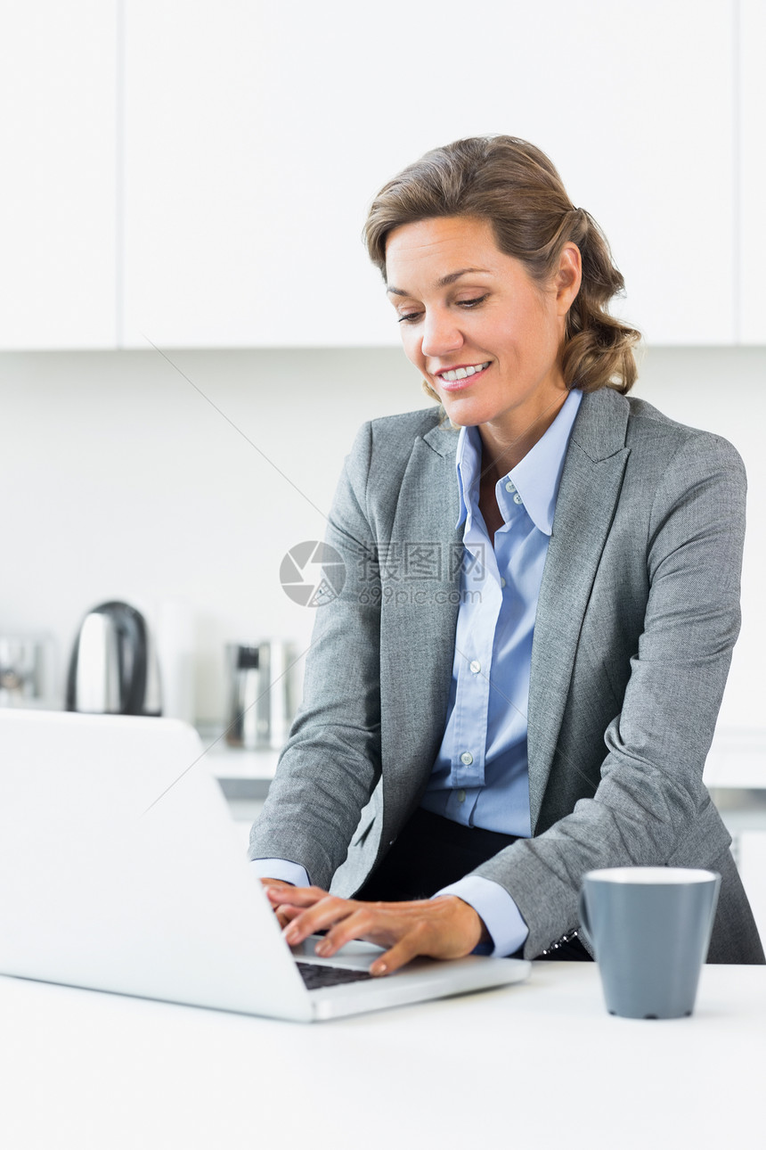 快乐的女人在笔记本电脑上打字女士套装棕色厨房人士微笑房子公寓家庭技术图片