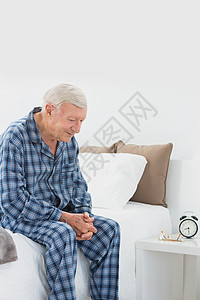 坐在床上的年长男子房子棉被睡衣男人闹钟头发白色桌子卧室羽绒被白色的头发高清图片素材