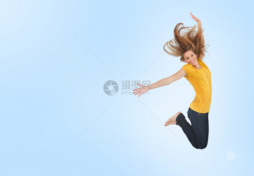 美丽的年轻女子为欢乐而跳跃幸福乐趣青年赤脚女性牛仔裤蓝色背景女士自由图片