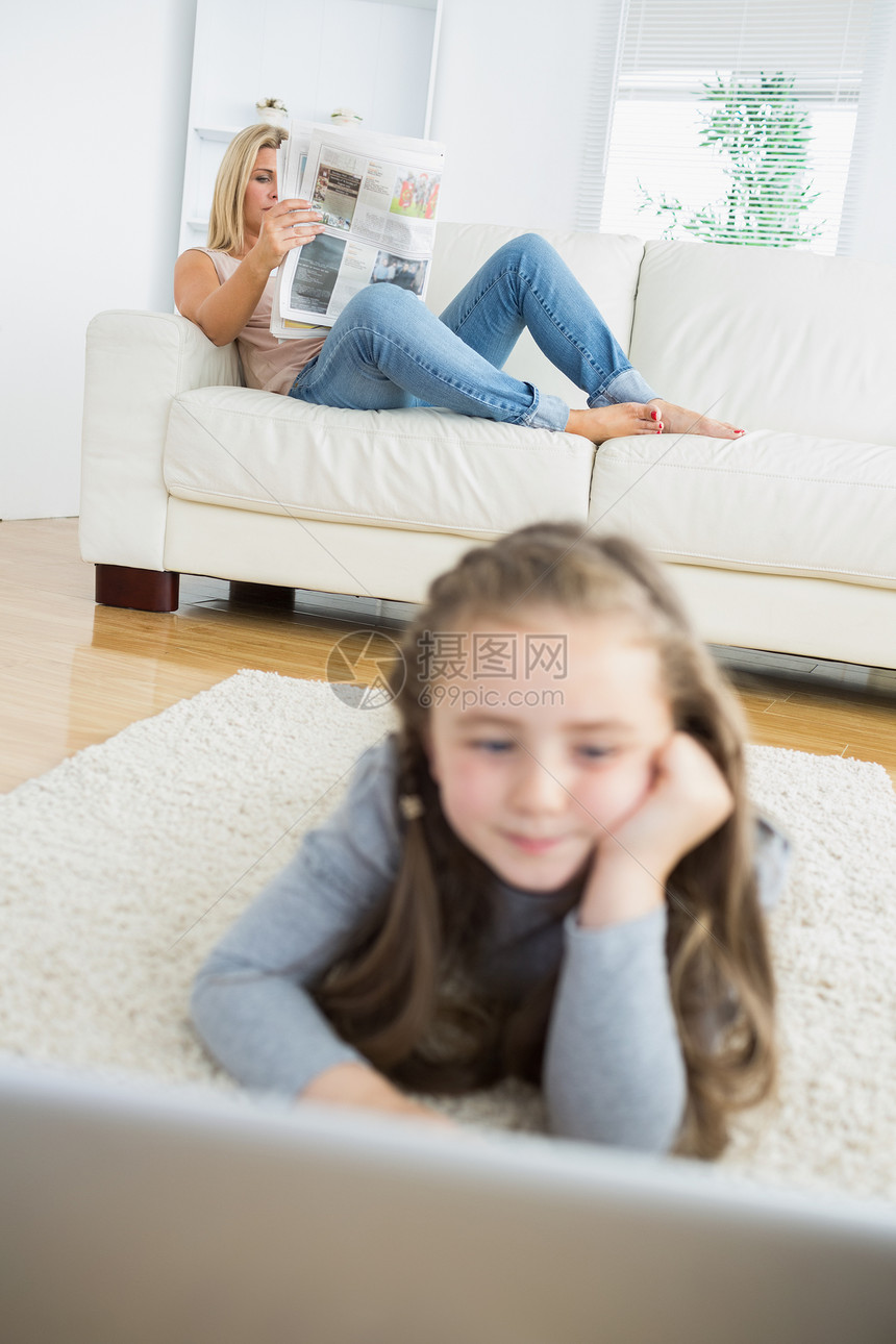 女孩与母亲一起使用笔记本电脑阅读报纸图片