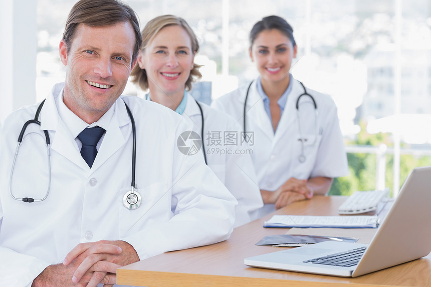 快乐的一群医生在他们的书桌上摆姿势图片