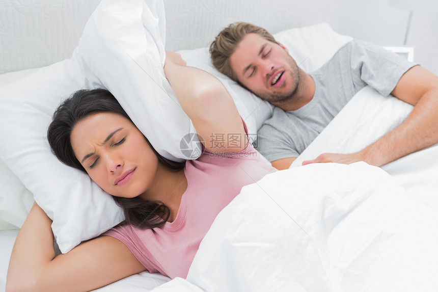 女人用枕头遮住她的耳朵 而丈夫在打呼噜图片