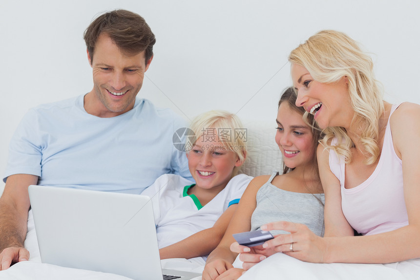 家庭在床上使用计算机和信用卡的家庭图片