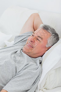 快乐的男人在床上放松男性公寓微笑棉被枕头卧室退休岁月坐垫家庭背景图片