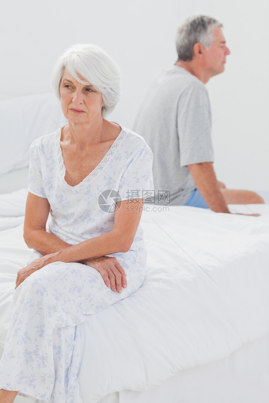 冲突期间愤怒的女人在床上哭泣退休男人争议女士卧室烦躁家庭住所睡衣白色图片