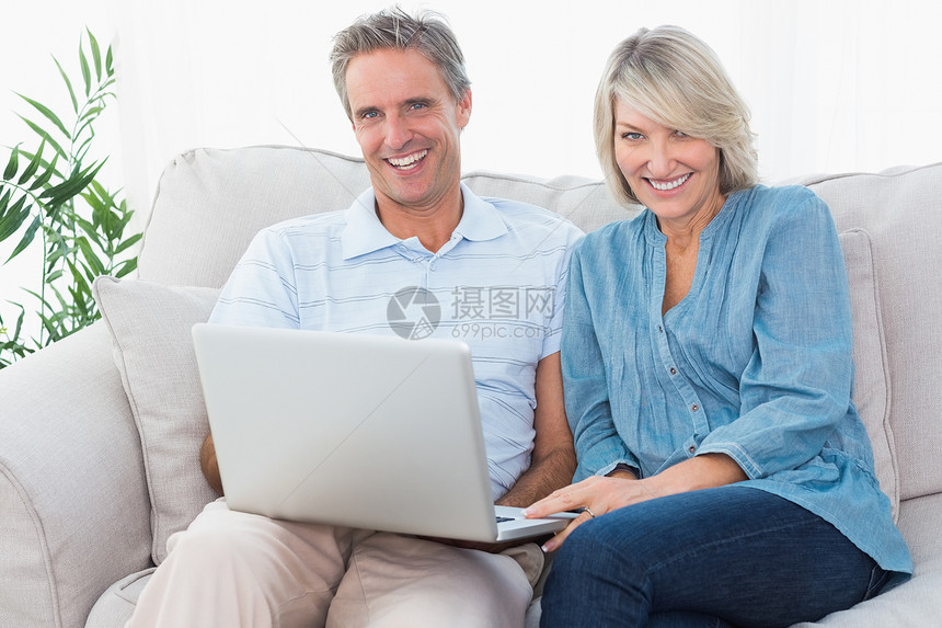 幸福的一对夫妇在沙发上一起用笔记本电脑看着Carmer图片