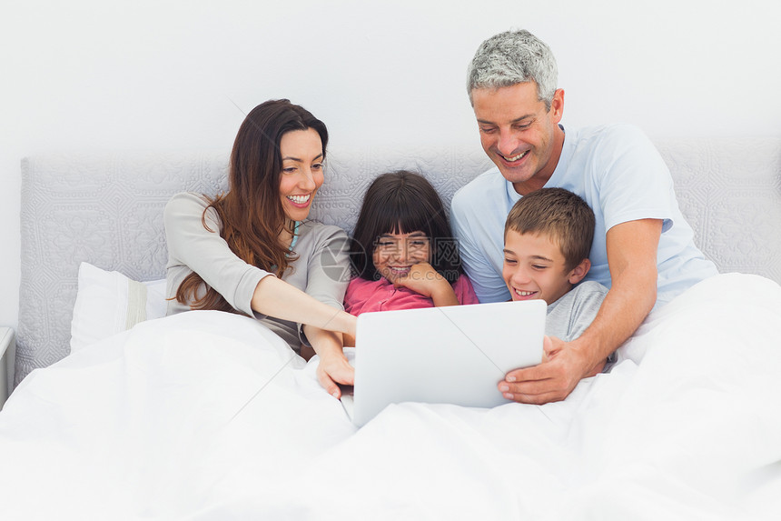 使用笔记本电脑躺在床上的微笑家庭男性儿子头发父亲房子羽绒被母亲短发快乐女士图片
