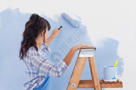 妇女用涂漆滚滚来油漆墙背景图片