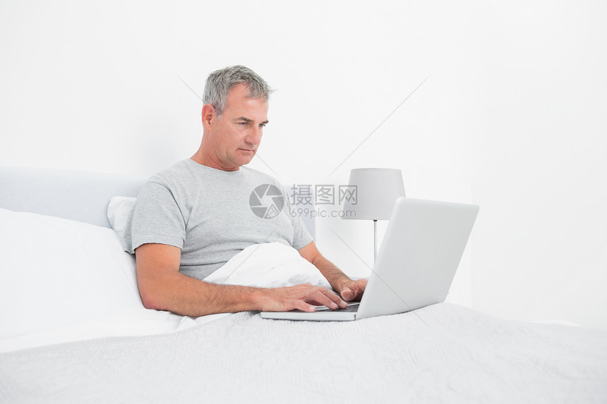 在床上使用笔记本电脑的灰色头发男子图片