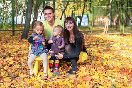 女人和叶子年轻的父母带着两个小女儿在黄秋公园享受天气背景