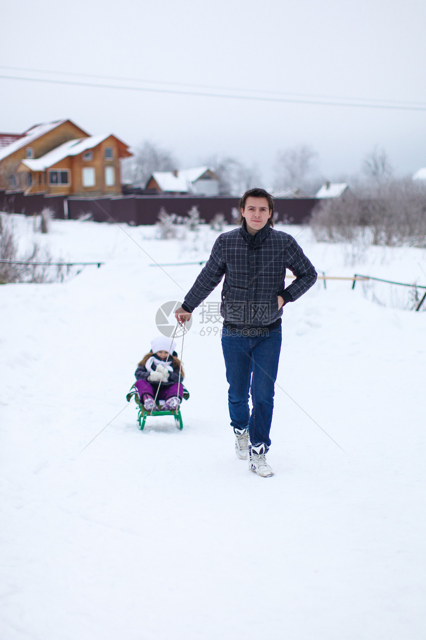 小爸爸在雪地外的雪橇上 卷起他可爱的小女儿男人父母乐趣家庭微笑成人快乐父亲季节闲暇图片