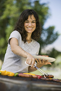 科罗娜快乐的年轻女子在公园烧烤的肖像女士拉丁收腰准备野餐假期女性娱乐炙烤盘子背景