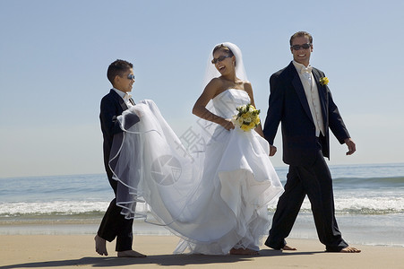与兄弟在海滩上散步的新娘和Groom高清图片