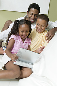 父亲与儿子和女儿在客厅看便携式DVD播放机的电影背景图片