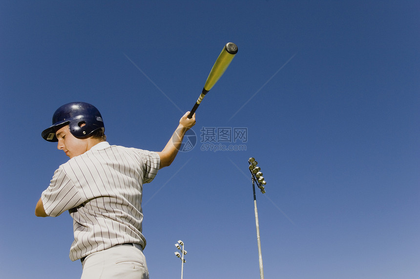 年轻棒球运动员在蓝天上挥棒图片