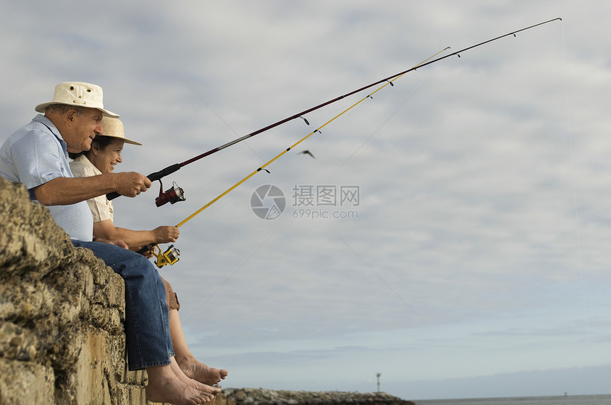 快乐的老年情侣在云天钓鱼的侧面景象图片