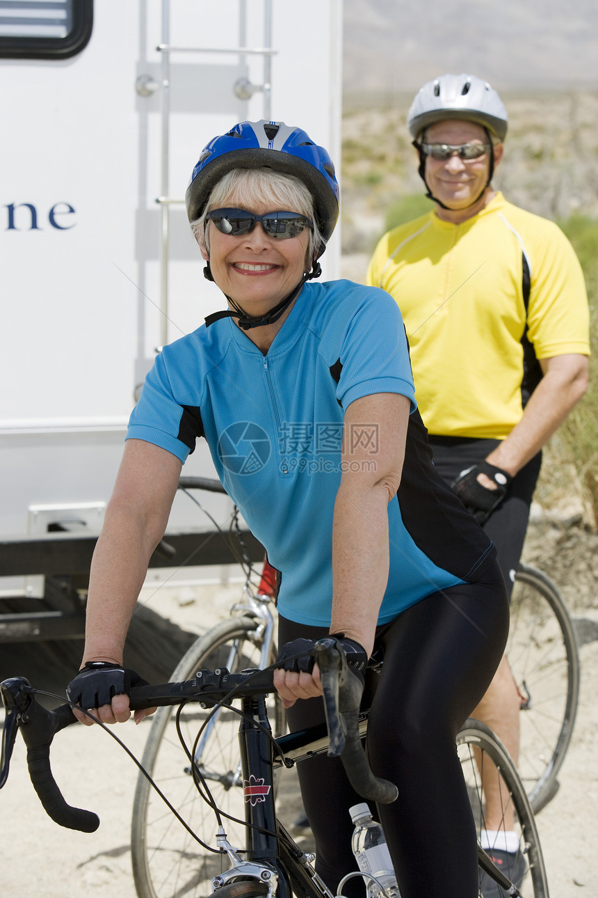 快乐的年长妇女与背景男子一起骑自行车的肖像图片